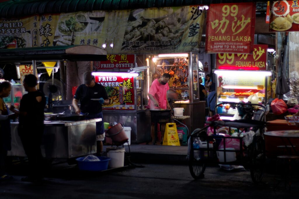 Suasana malam hari yang ramai di pusat kuliner jalanan atau street food hawker center di Penang, Malaysia.